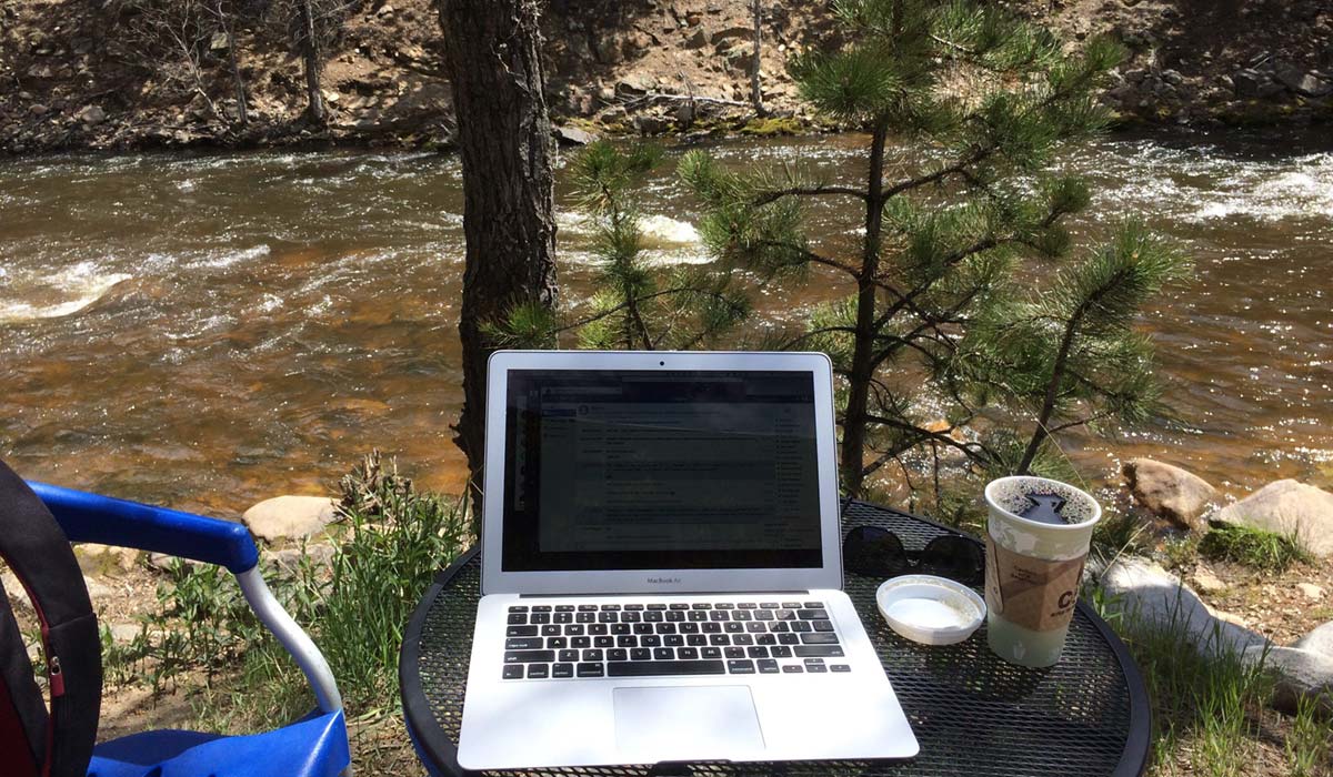 A photo of a coffee and laptop alongside a river